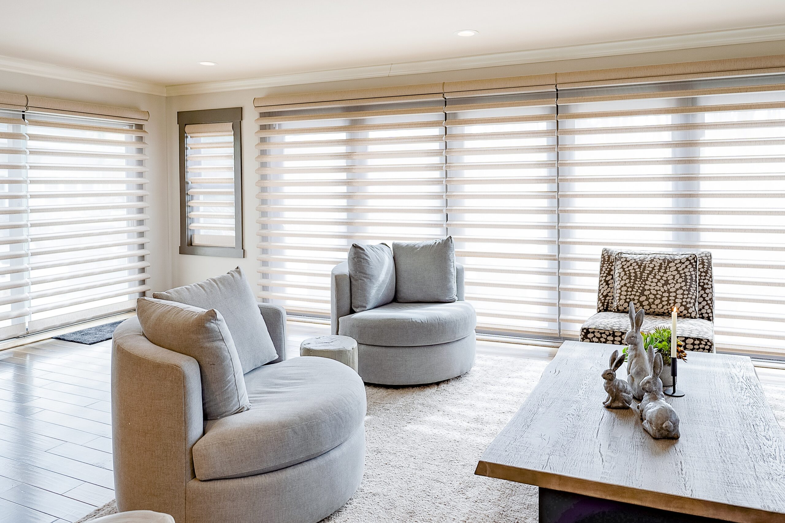 Sun is diffused by side-by-side Pirouette sheer shades in an open living room with grey trim windows