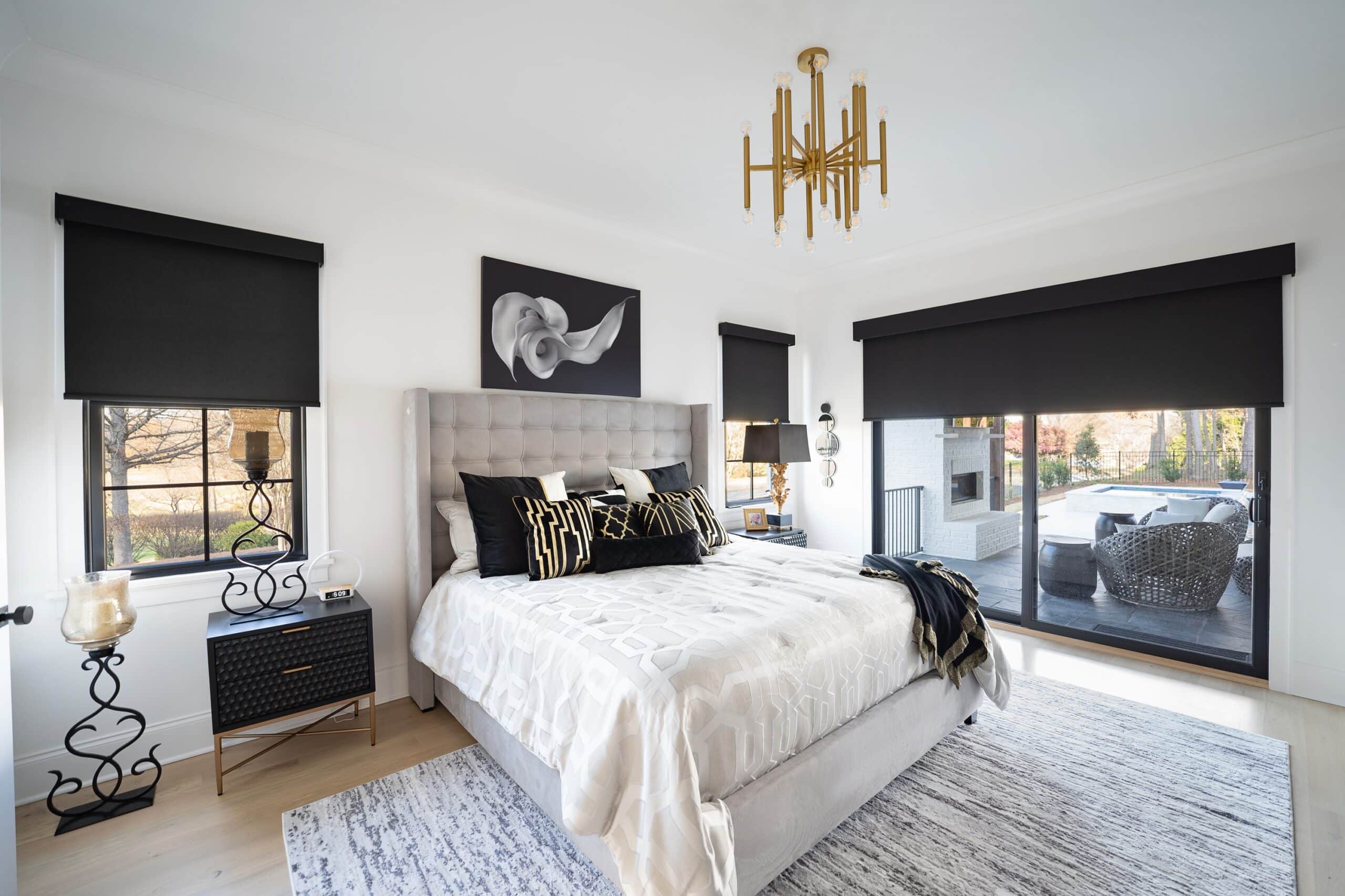 Black roller shades in a luxe-modern open master bedroom with a sliding door to a pool area