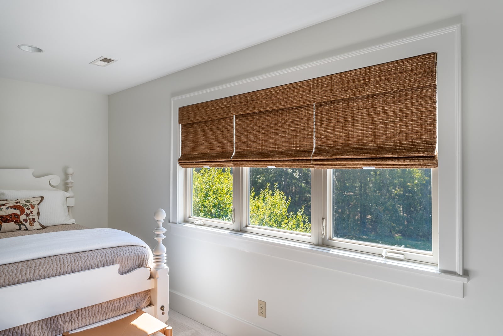 Stacking brown woven wood shades with cordless feature in a bedroom window