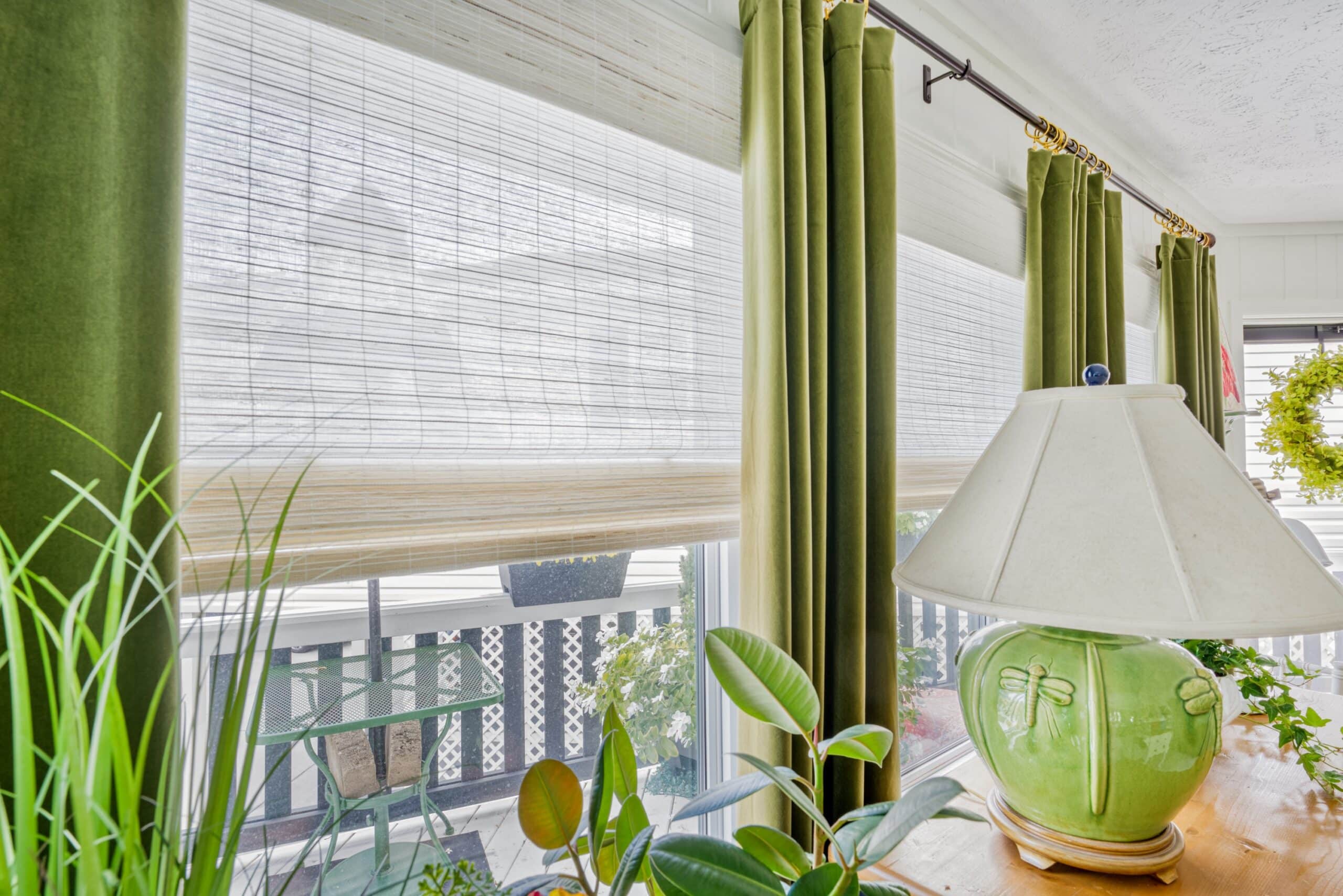 Side by side woven wood shade close up with green drapery and plants