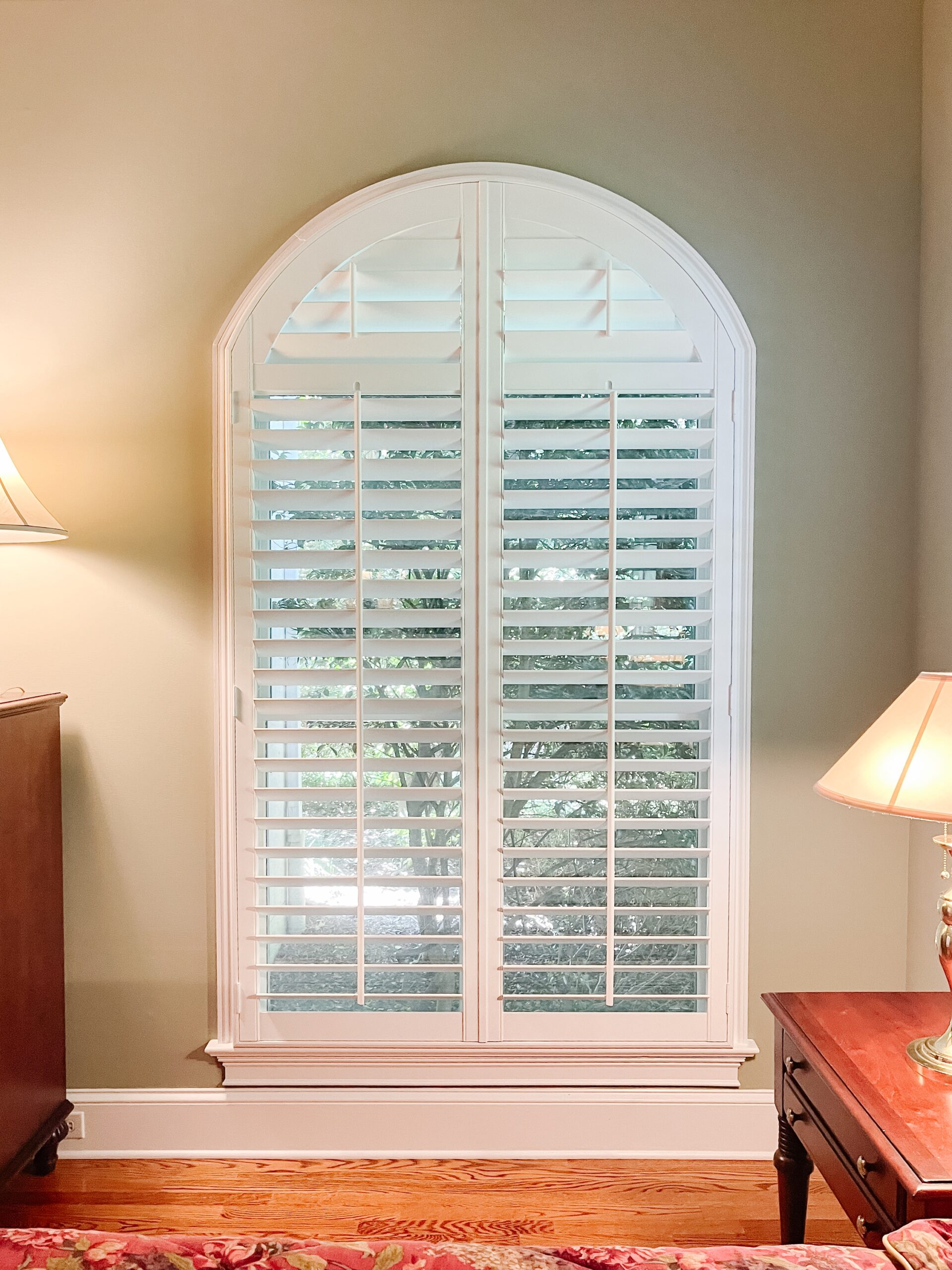 A white shutter on a window of a traditional bedroom in a home with green painted walls