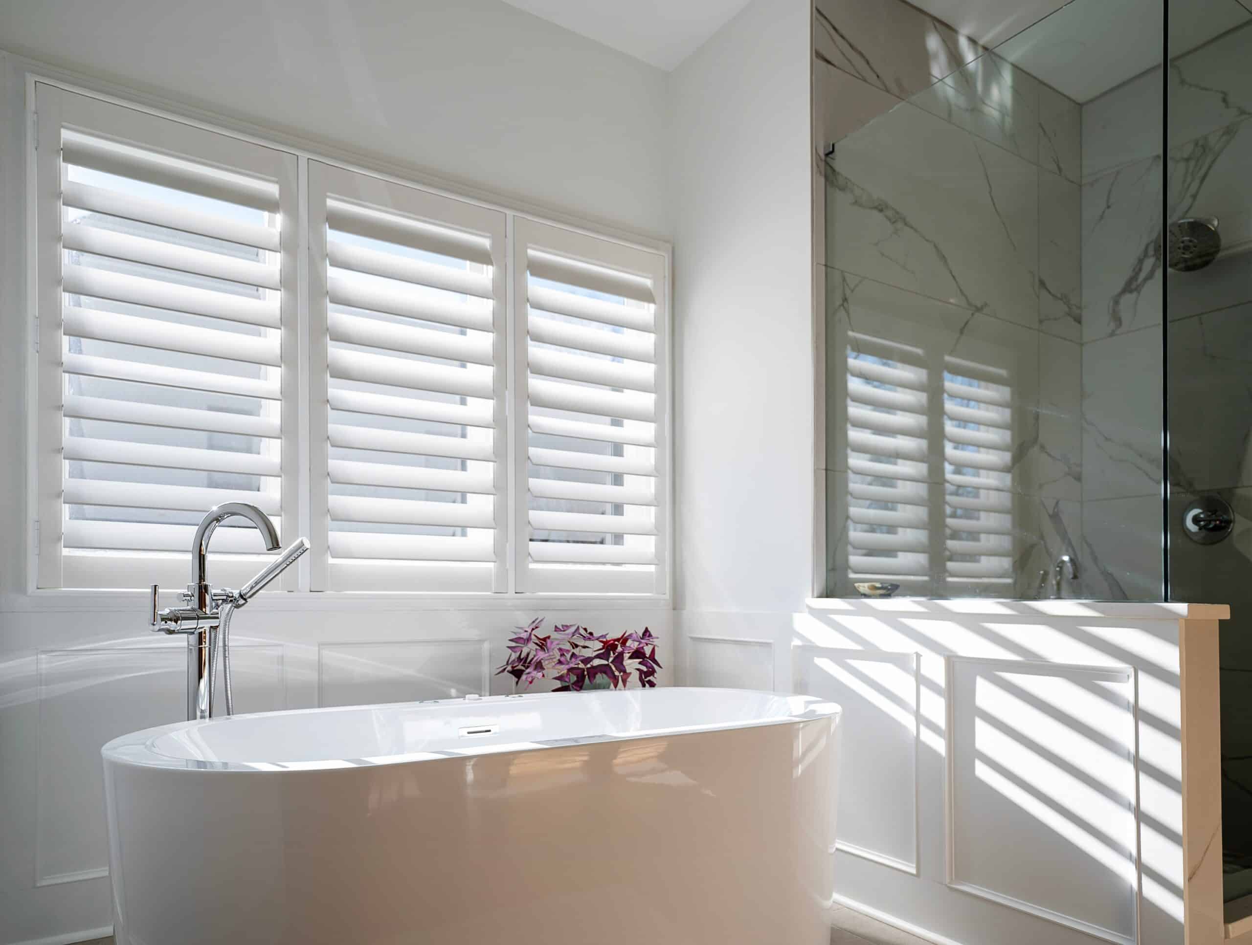 A modern bathroom with shutters above a tub