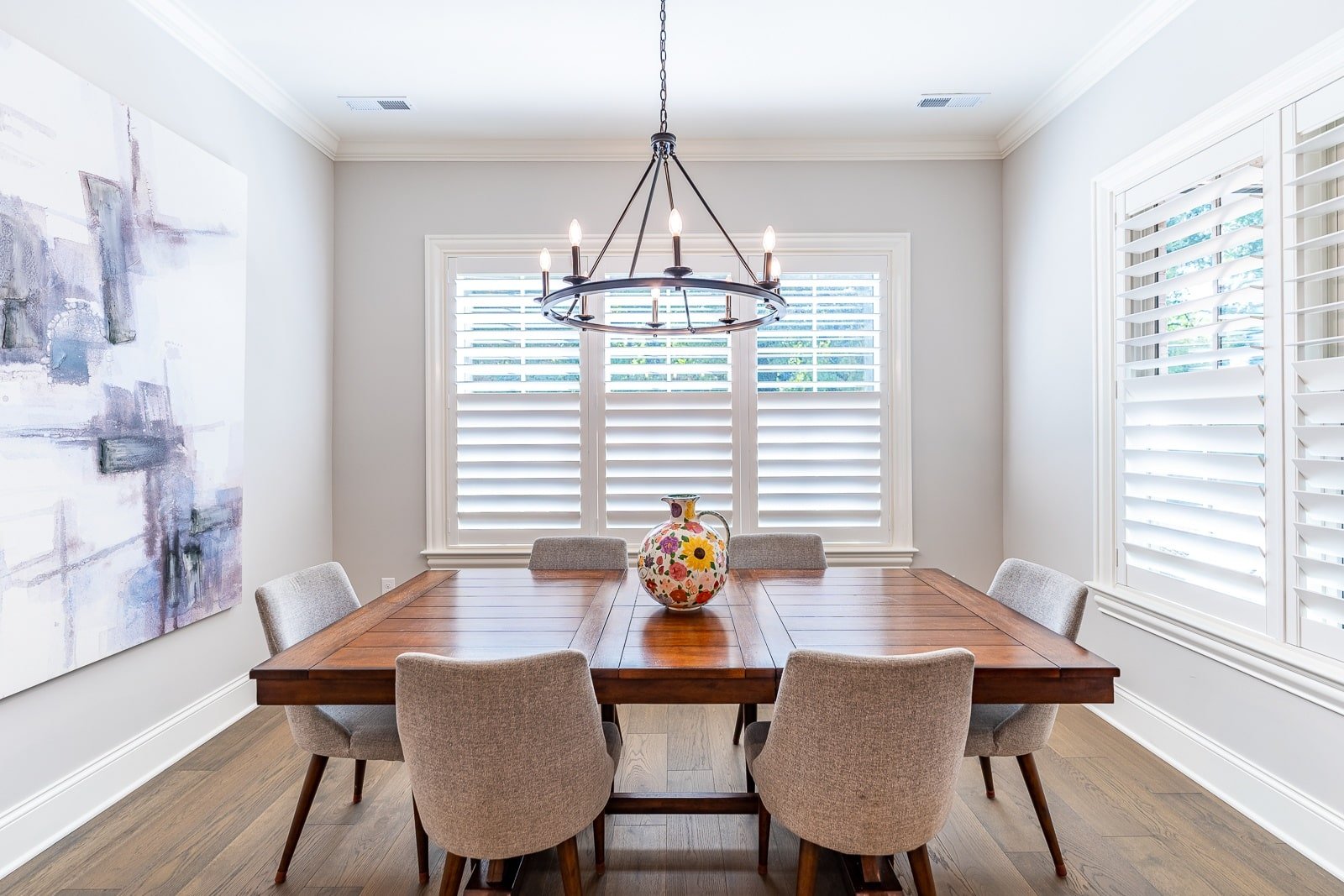 A dining area with a wood table, modern artwork and wood shutters