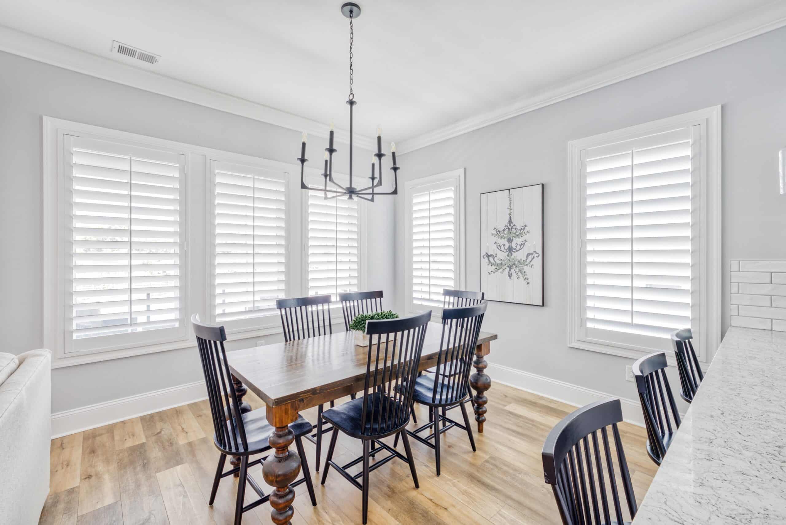 A well lit contemporary dining room with a dining room table surrounded by plantation shutters