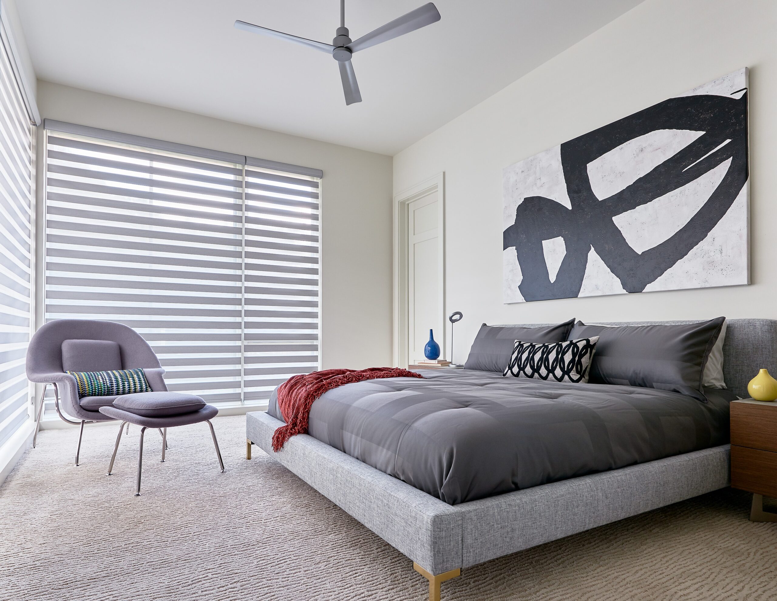 Minimalist bedroom with banded zebra shades, a gray chair, and a neutral-toned bed