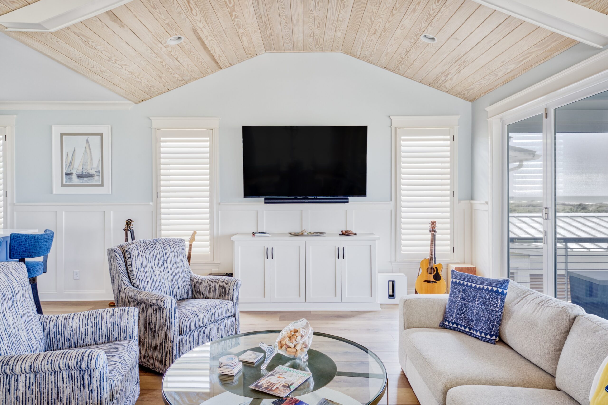 A modern open living room with plantation shutters and a sliding glass door with an ocean view