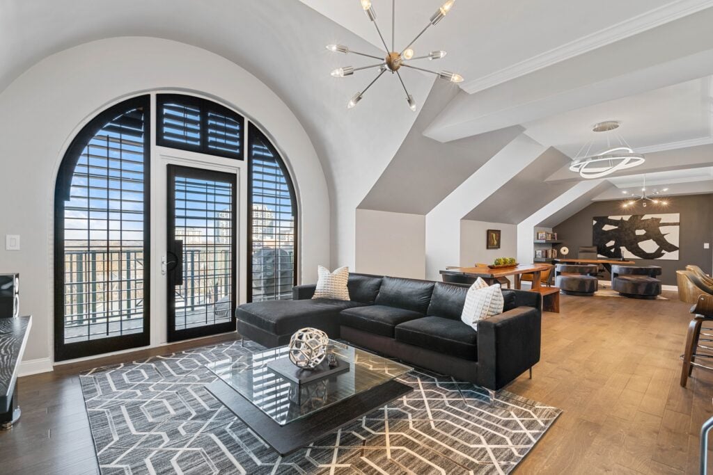 A modern condo features a large arched window and door, both framed by custom black wooden shutters for a striking contrast