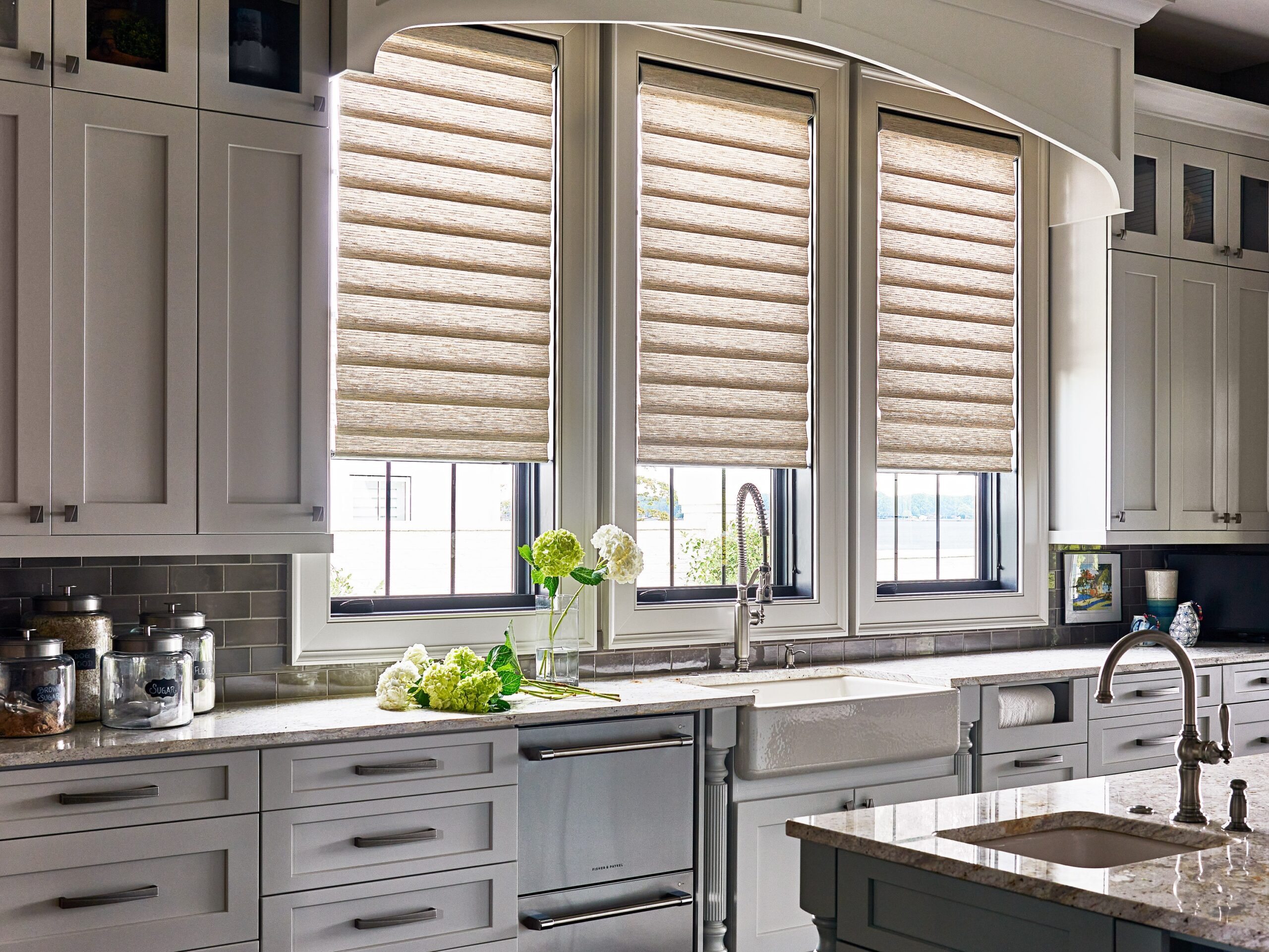 Elegant kitchen with textured roman shades, white cabinets, and a bouquet of hydrangeas on the countertop