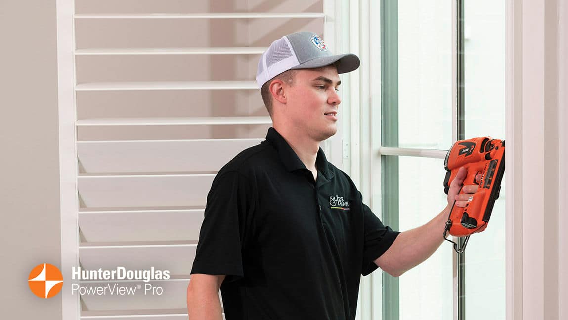 A blinds installation technician carefully nails a plantation shutter into place