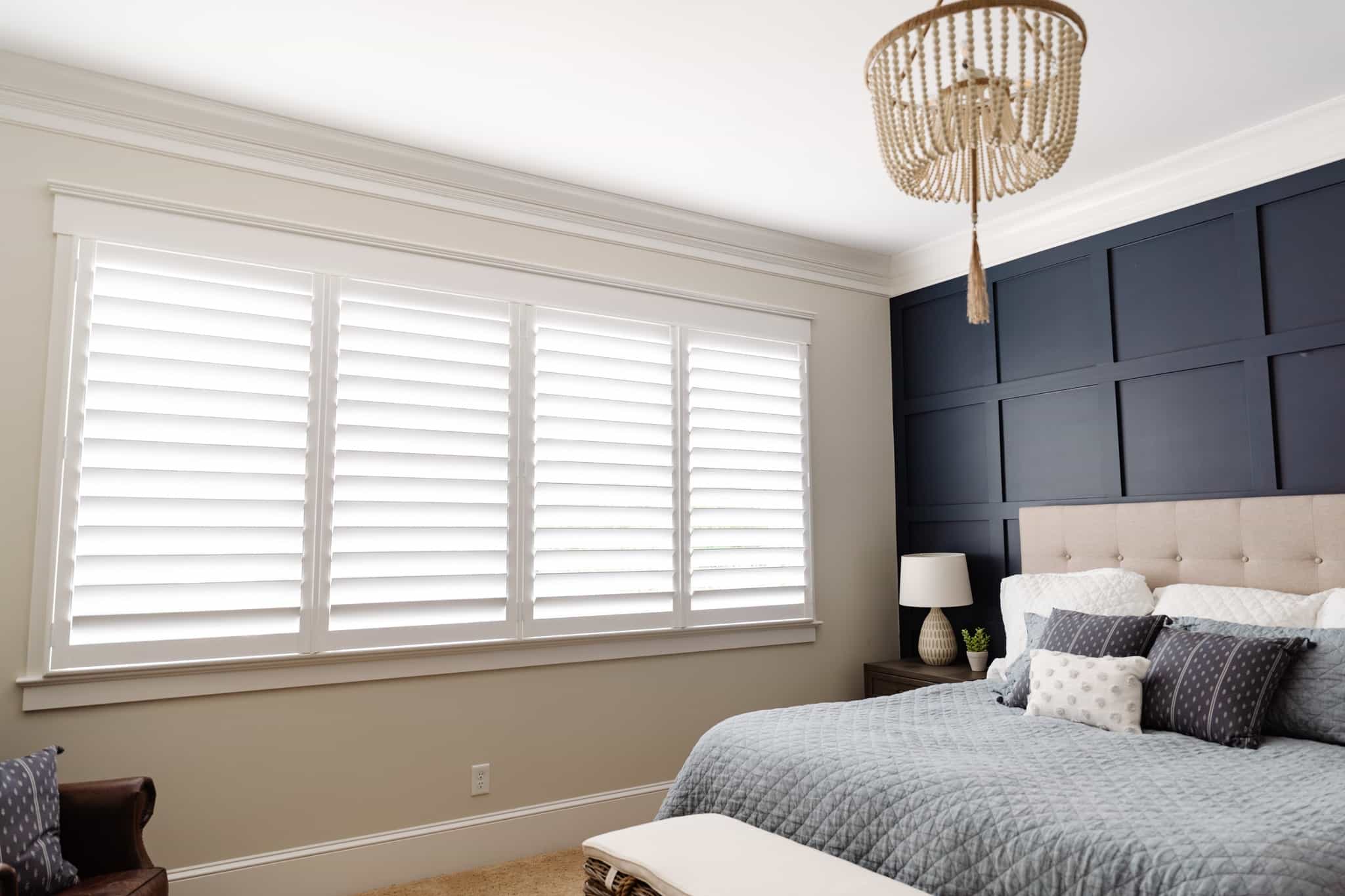 Primary bedroom with a boho chandelier, blue bedding, and white window shutters