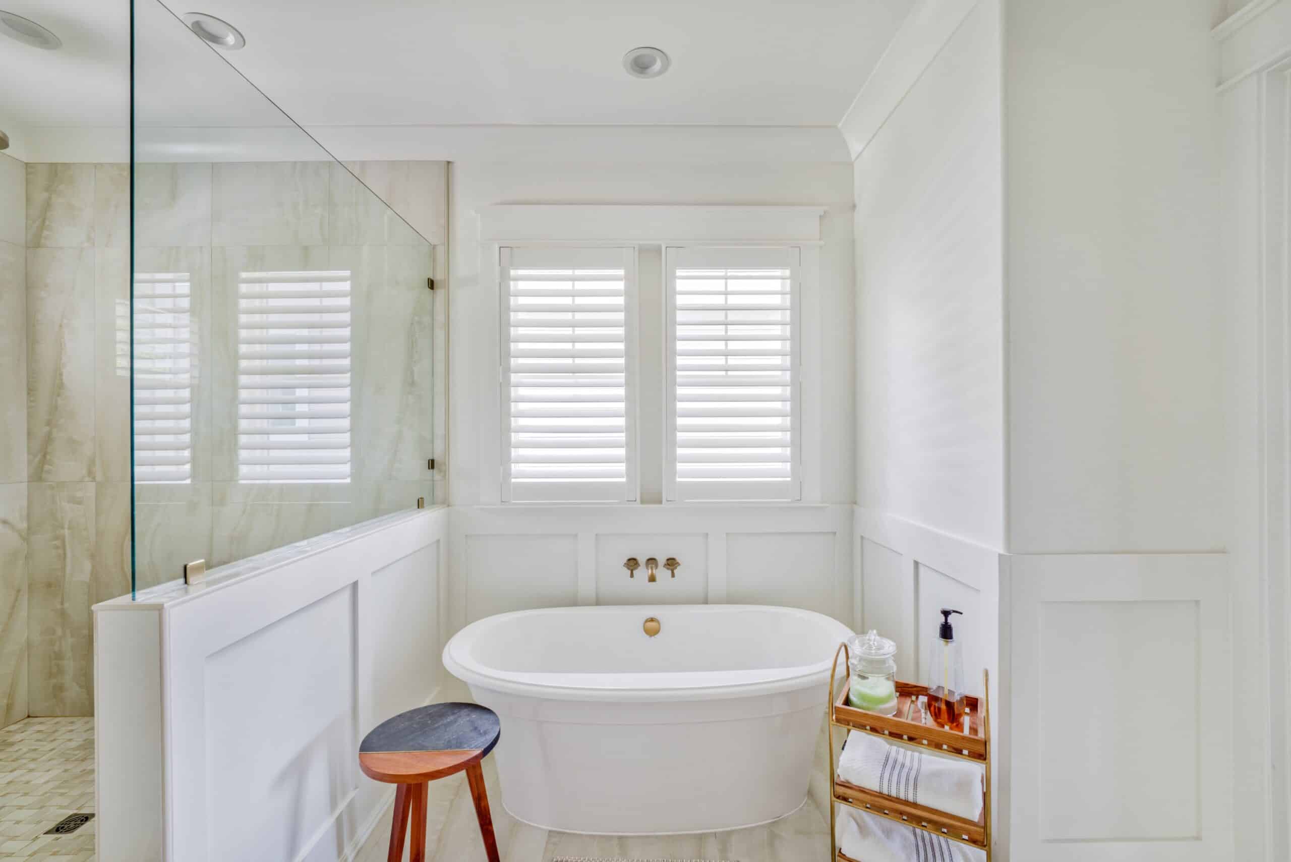 A white modern bathroom with plantation shutters over a free standing tub