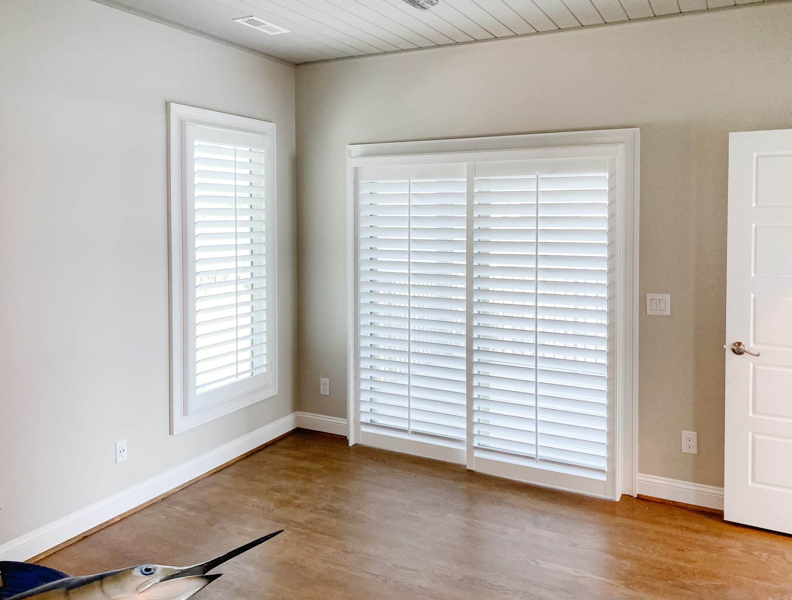 A single window on a wall adjacent to a sliding glass door that is covered by a sliding plantation-style shutter panel.