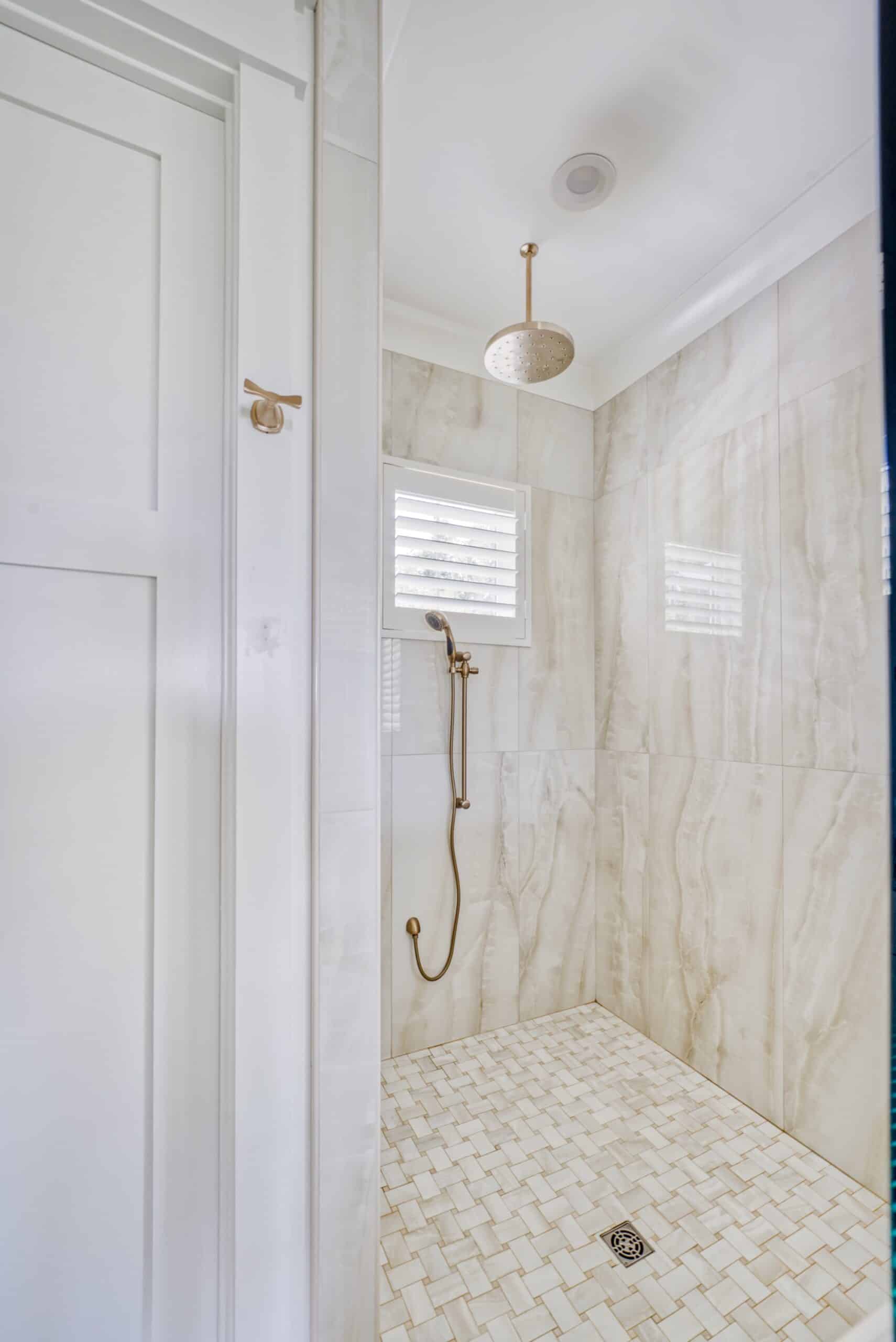 A small hidden tilt plantation shutter installed on tile in a modern shower with a rainfall showerhead