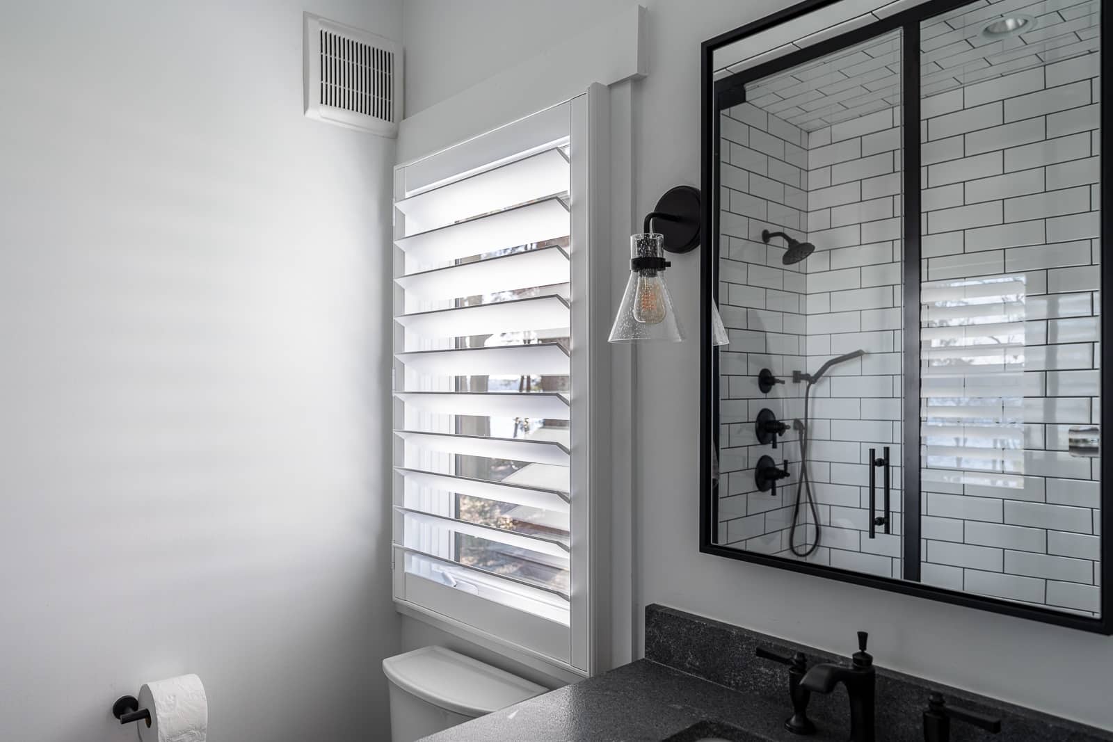 Bathroom with white subway tile and white shutter above toilet