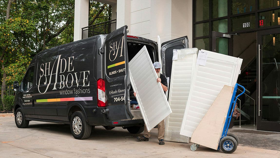 An installation technician unloads wood shutter panels from an A Shade Above van in preparation for install in a new home