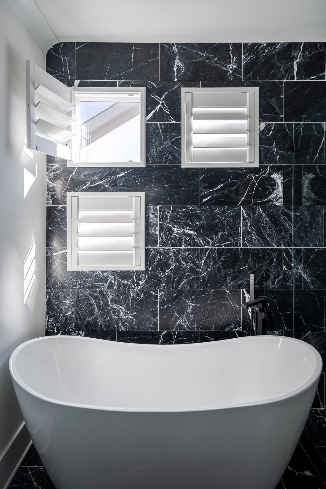 Small windows with shutters installed on tile above a tub