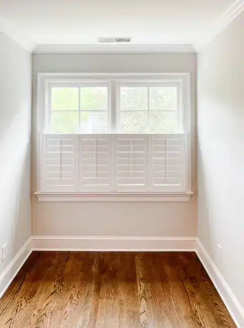 Cafe Shutters installed by A Shade above cover half of a window in a home office with hardwood floors