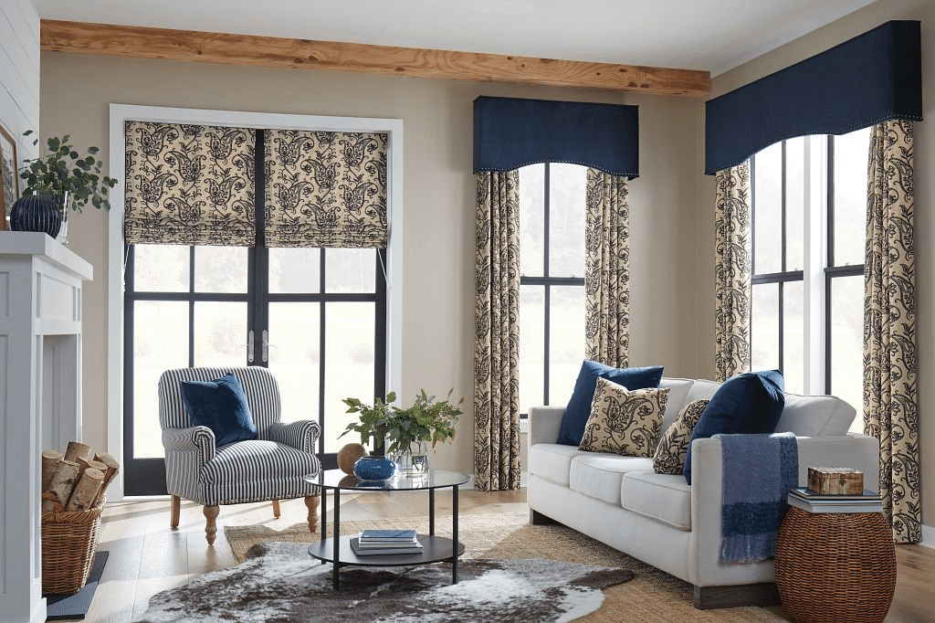 A transitional farmhouse living room with exposed wood beams and arch cornices atop floral drapery.