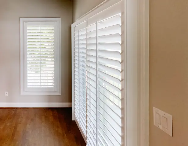 White Sliding Track Panel Shutters cover a sliding glass door in a primary bedroom.