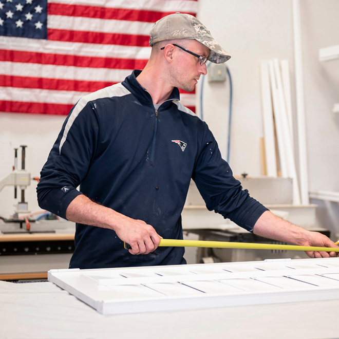 A worker measures and assembles a plantation shutter to its frame.