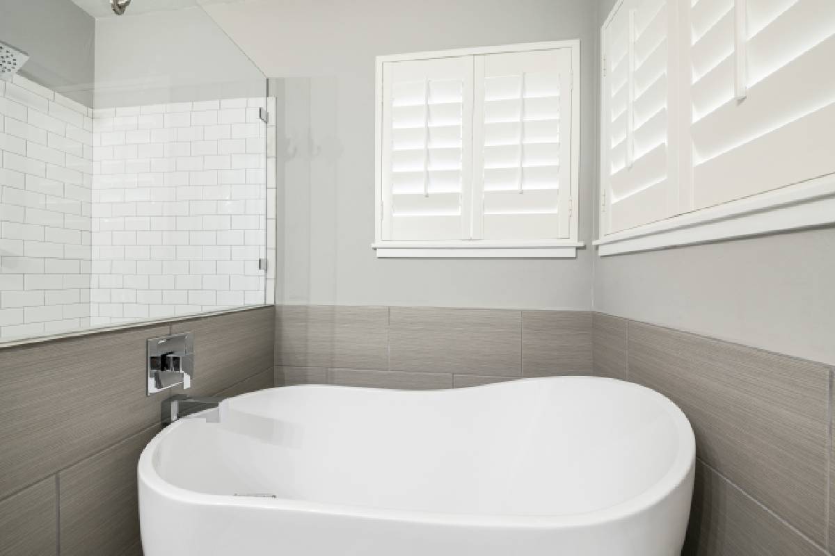 Sleek modern bathroom with a large white tub and white shutters