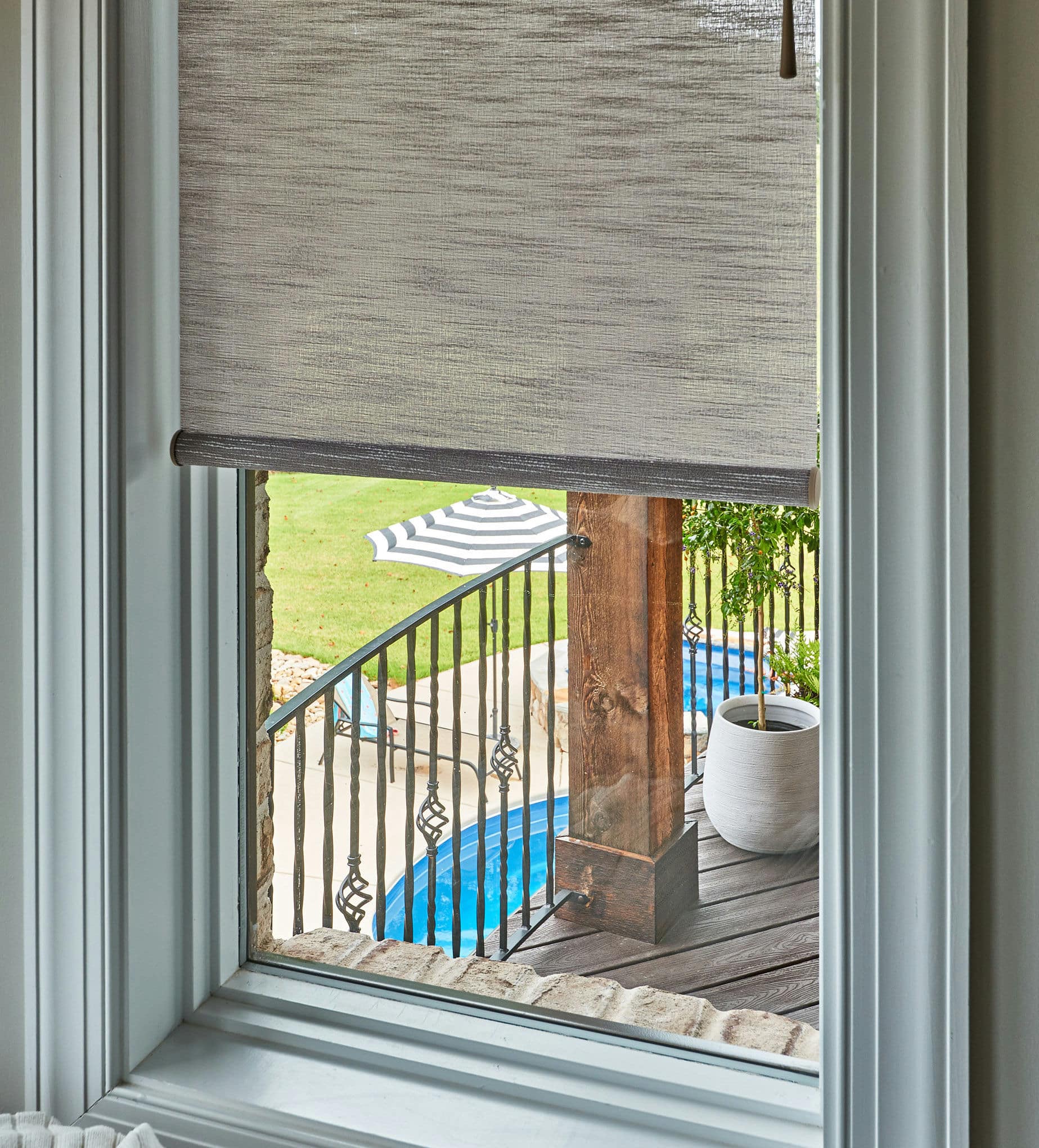 Gray textured roller shade covering a window overlooking an outdoor patio and swimming pool in a Cary, North Carolina home.