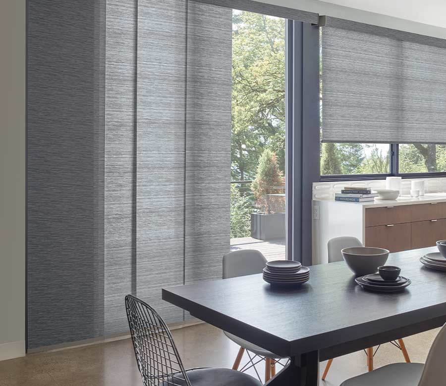 gray panel track blinds over sliding glass door in kitchen with matching roller shades on windows